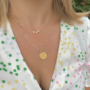 May include: A gold necklace with a small round pendant featuring a constellation design. The necklace is layered with a delicate chain with three small star charms.
