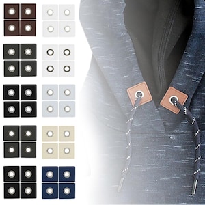 Könnte beinhalten: Ein Satz mit 10 Metallösen in verschiedenen Farben, darunter Braun, Weiß, Beige, Schwarz und Blau. Die Ösen sind in Reihen zu vieren angeordnet, wobei jede Reihe eine andere Farbe aufweist. Die Ösen werden häufig für Kleidung und Bastelarbeiten verwendet.