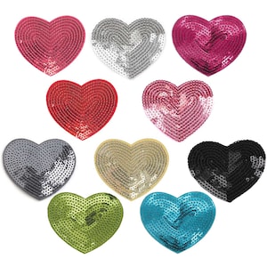 Könnte beinhalten: Zehn herzförmige Pailletten-Patches in verschiedenen Farben, darunter Rot, Pink, Silber, Gold, Schwarz, Grün und Blau. Die Pailletten sind in einem kreisförmigen Muster angeordnet, wodurch ein strukturierter Look entsteht.