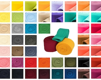 Op de afbeelding: Een selectie van gerolde stoffen in verschillende kleuren, waaronder beige, geel, groen, blauw, rood, oranje, roze, paars, bruin, grijs en zwart.