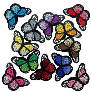 Könnte beinhalten: Eine Sammlung von gestickten Schmetterlingsaufnähern in verschiedenen Farben, darunter Blau, Grün, Gelb, Rot und Lila. Jeder Aufnäher hat detaillierte Flügelmuster und einen schwarzen Rand. Die Aufnäher sind auf weißem Hintergrund angeordnet.