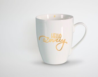 May include: White ceramic mug with a curved handle. The mug features the gold text "HELLO lovely" and two small gold hearts inside the rim. The mug is a simple, elegant design.