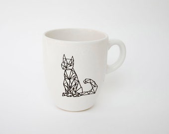May include: White ceramic mug with a black geometric cat design. The cat is depicted in a sitting position, created from interconnected triangles and lines. The mug has a curved handle and a smooth, glossy finish.