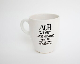 May include: White ceramic mug with a curved handle. The mug features black text that reads "ACH WIE GUT DASS NIEMAND WEISS AUF wen & was ICH ALLES SCHEISS".