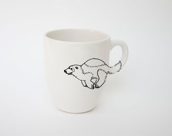 May include: White ceramic mug with a black line drawing of a running polar bear. The bear's body is on the side of the mug, with the tail extending to the handle. The mug has a simple, clean design.