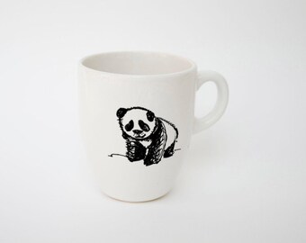 May include: White ceramic mug with a black and white panda bear illustration. The panda is drawn in a simple, sketch-like style. The mug has a curved shape and a handle on the right side.