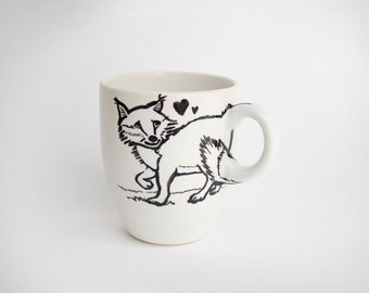 May include: White ceramic mug featuring a black and white illustration of a fox with two hearts above its head. The mug has a rounded handle and a simple, clean design, perfect for coffee or tea.