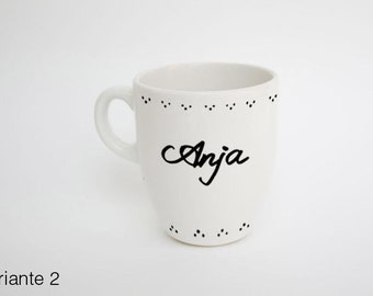 May include: White ceramic mug with a handle, featuring the name "Anja" in black script. The mug has a dotted design around the top and bottom rims. The mug is on a white background.