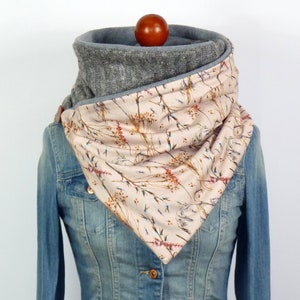 Könnte beinhalten: Grauer und floral gemusterter Cowl-Schal. Der Schal hat einen grauen Strickkragen und einen beigen Stoff mit floralem Design. Der Schal wird auf einer Jeansjacke präsentiert. Der Schal ist ein gemütliches Accessoire.