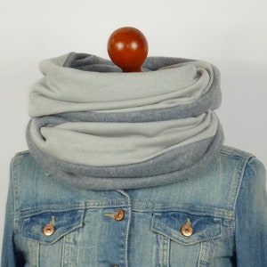 Peut inclure: Une écharpe infinie grise et gris clair en polaire. L'écharpe est pliée et exposée sur un mannequin.