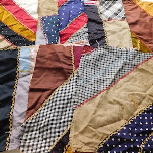 May include: A patchwork quilt made of various fabrics, including gingham, polka dot, and solid colors. The quilt is sewn together with a gold thread and has a rustic, vintage aesthetic.