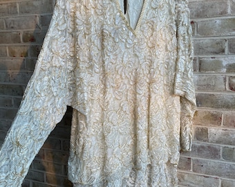 May include: A white lace top with gold embroidery. The top has a V-neck and long sleeves. The label reads "Judith Ann Plus".