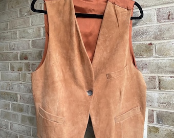 May include: A tan suede vest with a satin back and lining, featuring a single button closure and two front pockets. The vest is hanging on a black hanger. The brand name "KENAR" is visible on the satin lining.
