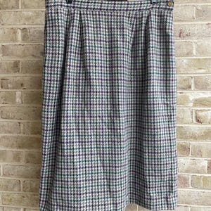 May include: A knee-length skirt with a houndstooth pattern in shades of gray, purple, and green. The skirt is hanging on a black hanger. The fabric appears to be a woven material.