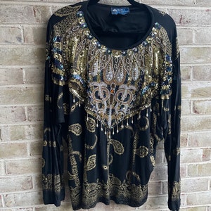 May include: Black long-sleeved shirt with a gold and silver sequined design. The shirt has a paisley pattern and a round neckline.