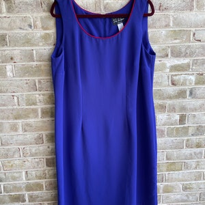 May include: A sleeveless royal blue dress with a red trim around the neckline. The dress has a simple, fitted silhouette and is made of a smooth, silky fabric. The dress has a label that reads "S.L.Fashions".