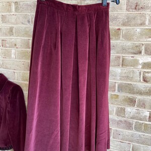May include: A burgundy velvet skirt with pleats. The skirt is hanging on a hanger and has a simple design.