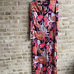 May include: A long, purple maxi dress with a floral print in shades of pink, orange, and white. The dress has long sleeves and a scoop neck.