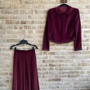 May include: A burgundy velvet skirt and matching jacket with a ruffled hem. The skirt is pleated and the jacket has a Peter Pan collar and button closure.