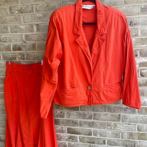 May include: A bright orange skirt and blazer set. The blazer has a single button closure and a pocket on each side. The skirt is a-line and falls to the knees.