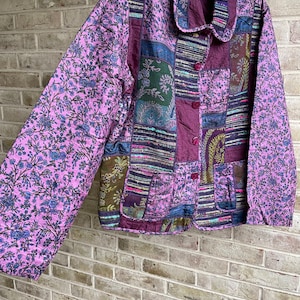 May include: A purple, pink, and green patchwork jacket with a floral print. The jacket has a collar and button closure.
