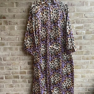 May include: A long-sleeved robe with a leopard print pattern in shades of brown, purple, and white. The robe has a button-up front and a collar.