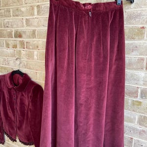 May include: A burgundy velvet skirt and matching cropped jacket with a ruffled hem. The skirt has a zipper closure and a high waist.
