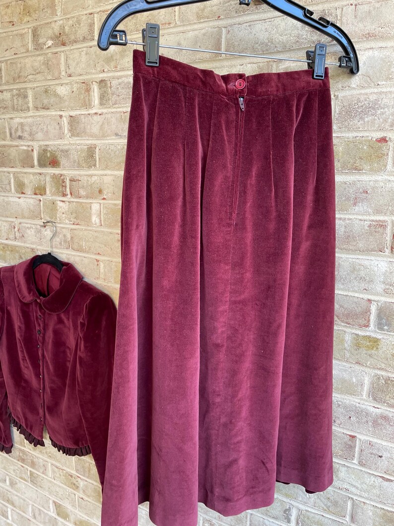 May include: A burgundy velvet skirt and matching cropped jacket with a ruffled hem. The skirt has a zipper closure and a high waist.