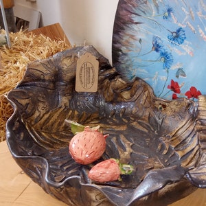 Peut inclure: Un bol en céramique avec un glaçage brun et doré, orné d'un motif de feuilles. Le bol est rempli de deux petites fraises en céramique rouge.