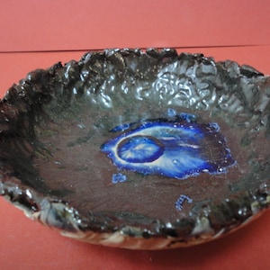 Könnte beinhalten: Eine dunkelbraune Keramikschale mit einem blauen und weißen Glasurdesign. Die Schale hat eine raue, strukturierte Außenseite und eine glatte Innenseite.