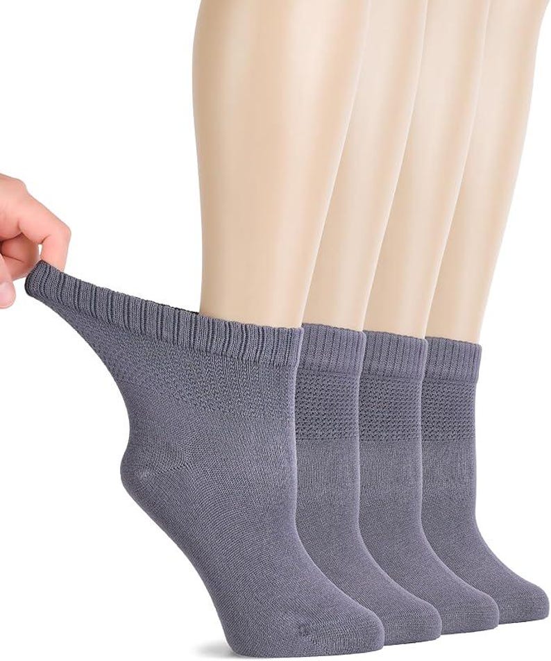May include: A set of four grey ankle socks featuring a ribbed cuff and a textured knit pattern on the upper section. The socks are shown in a row, with one being pulled slightly to display the stretch and the fabric texture of the material.