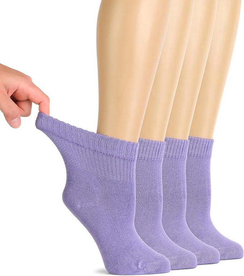 May include: A set of four ankle-length socks in a solid light purple color. Each sock features a ribbed cuff at the top and a smooth knit texture throughout the body, designed to sit just above the ankle bone for a standard fit and coverage.