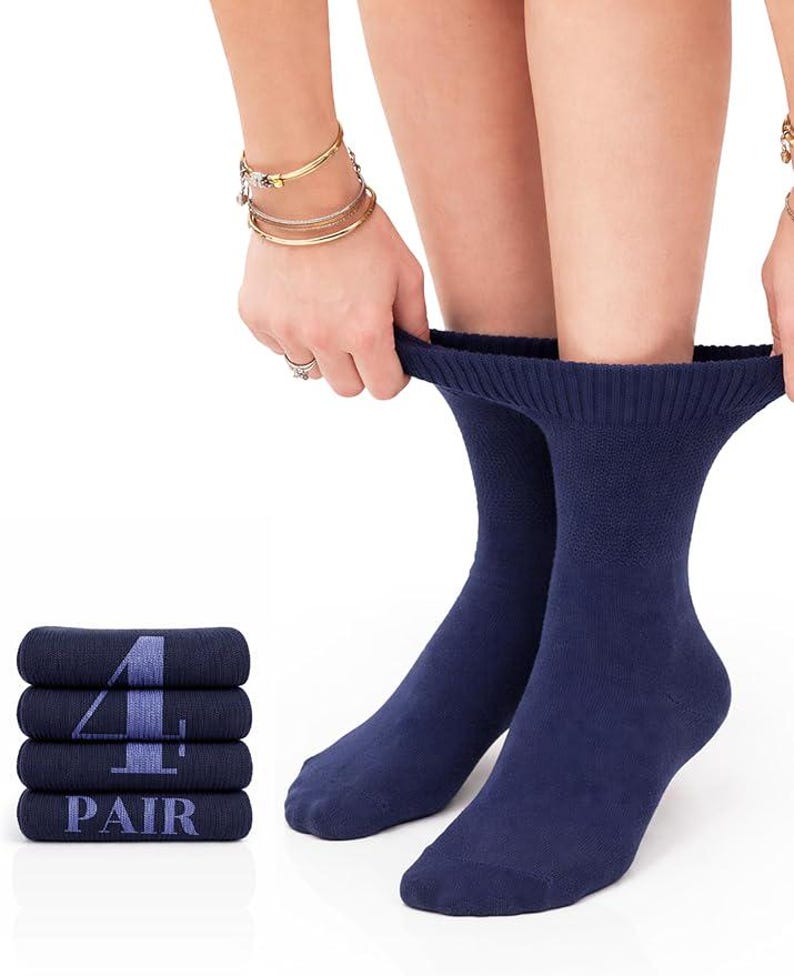 May include: A pair of solid navy blue crew socks with a ribbed cuff. To the left, a stack of four folded navy blue socks features the text "4 PAIR" printed in a light blue font across the front of the folded fabric, indicating a set of four.