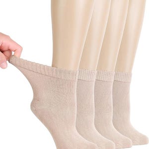 May include: A set of four ankle socks in a solid light beige color. Each sock features a ribbed cuff at the top and a standard knit construction. The socks are displayed on mannequin feet to show the fit and length, with one sock being pulled.