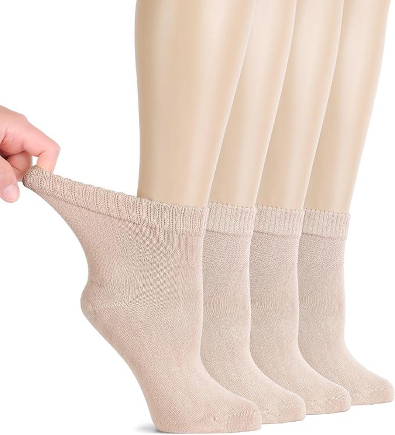May include: A set of four ankle socks in a solid light beige color. Each sock features a ribbed cuff at the top and a standard knit construction. The socks are displayed on mannequin feet to show the fit and length, with one sock being pulled.