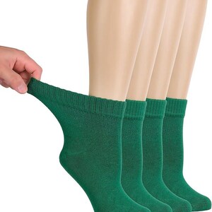 May include: A set of four solid dark green ankle socks featuring a ribbed cuff at the top. The socks are displayed in a row, with one sock being pulled slightly to the side to show the stretch and texture of the fabric. The material appears to be a knit textile.