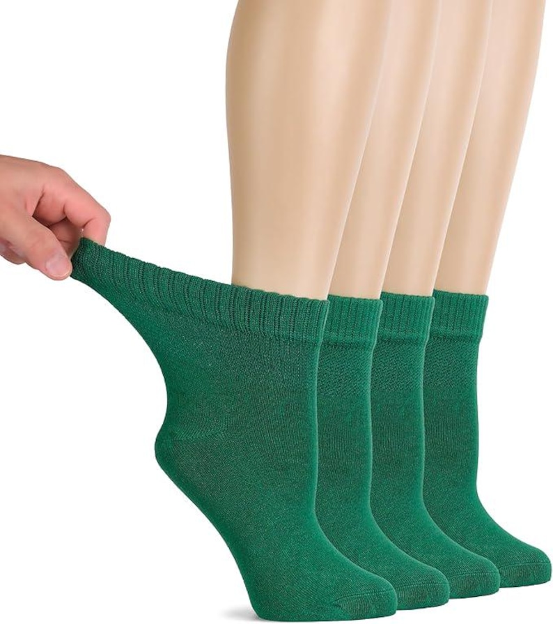 May include: A set of four solid dark green ankle socks featuring a ribbed cuff at the top. The socks are displayed in a row, with one sock being pulled slightly to the side to show the stretch and texture of the fabric. The material appears to be a knit textile.