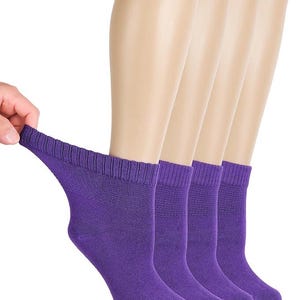 May include: A set of four purple ankle socks featuring a ribbed cuff design. The socks are displayed in a row, with one sock being held at the top edge to show the texture and stretch of the fabric. The material appears to be a solid, vibrant purple color.