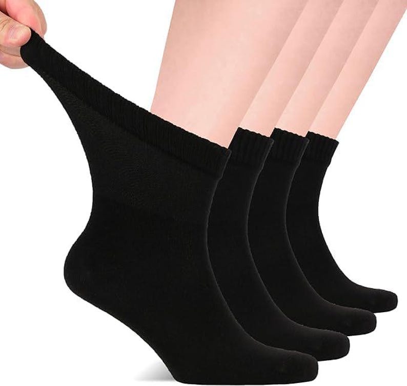 May include: A set of four solid black ankle socks featuring a ribbed cuff design. The socks are shown in a stacked arrangement, with the front-most sock being pulled slightly to demonstrate the stretch and texture of the fabric material.