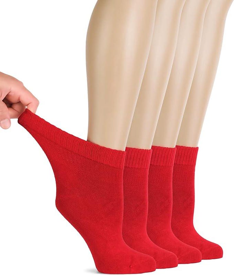 May include: A set of four solid red ankle socks featuring a ribbed cuff design. The socks are displayed on mannequin feet, with one sock being pulled slightly to show the stretch and texture of the fabric. The material is a consistent bright red.