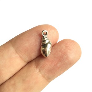 Peut inclure: Charme en forme de coquillage argenté. Le charme est en forme de coquillage avec un motif en spirale. C'est un petit charme, parfait pour ajouter à des bijoux ou des objets artisanaux.