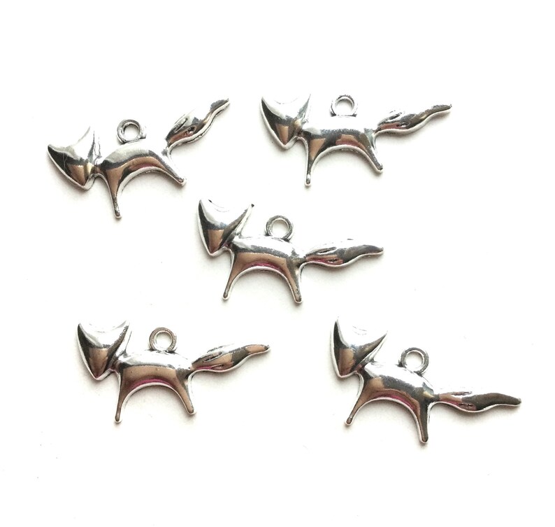 May include: Five silver fox charms with a simple, stylized design. Each charm has a loop for attaching to a necklace, bracelet, or other jewelry.