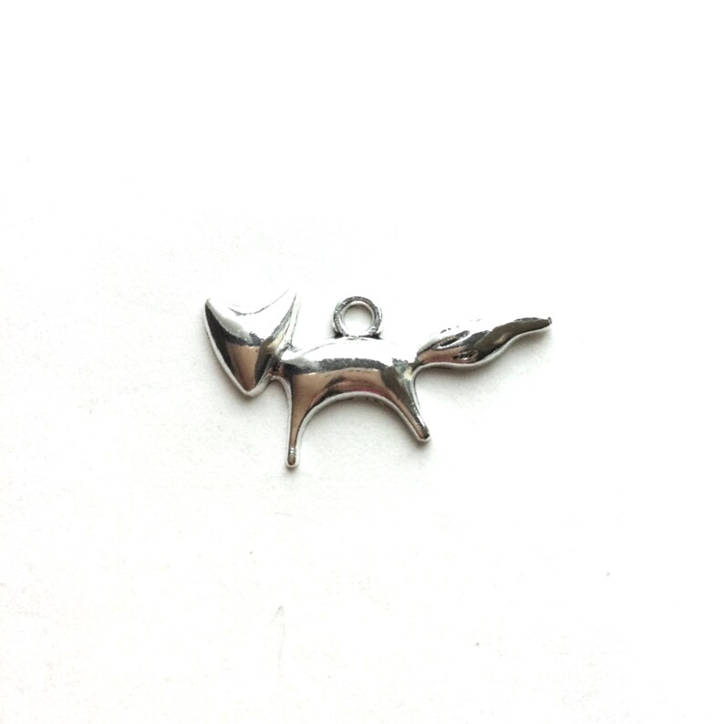May include: Silver charm in the shape of a stylized fox. The charm has a loop at the top for attaching to a necklace or bracelet.