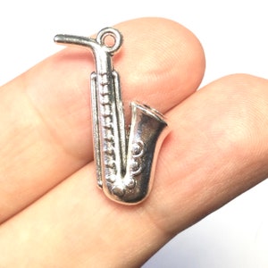 Peut inclure: Breloque en forme de saxophone argenté avec un design détaillé. Le breloque a une boucle en haut pour l'attacher à un collier ou un bracelet.
