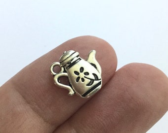 May include: Silver charm in the shape of a teapot with a floral design. The charm is small and detailed.