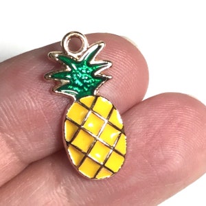 Peut inclure: Breloque ananas en ton or avec des feuilles vertes et de l'émail jaune. L'ananas est détaillé avec un motif en grille.