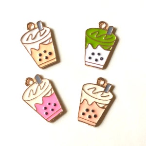 Peut inclure: Quatre pendentifs de charme en or en forme de tasses de bubble tea. Chaque charme a une couleur et une garniture différentes : blanc avec une garniture blanche, rose avec une garniture rose, vert avec une garniture verte et pêche avec une garniture pêche. Chaque charme a des perles de boba noires.