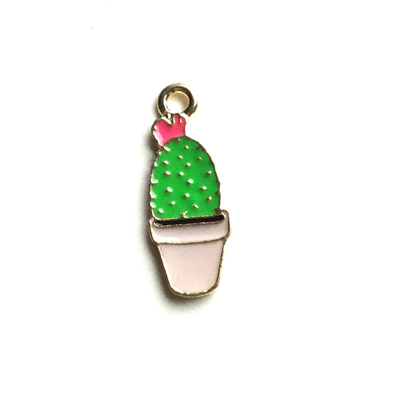 Pode incluir: Encanto de metal dourado com um cacto verde com uma flor rosa no topo, plantado em um vaso branco.