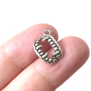 May include: Silver charm in the shape of a set of teeth. The charm is detailed with sharp points and a textured surface.