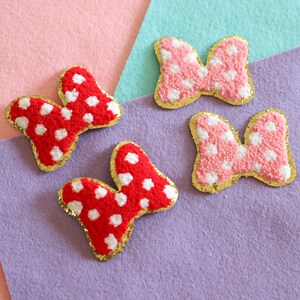 May include: Four fuzzy fabric bows with gold trim and white polka dots. Two bows are red and two are pink.
